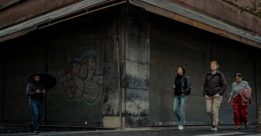 Pedestrians walk past a closed shop on a rainy city street, creating a candid urban scene.