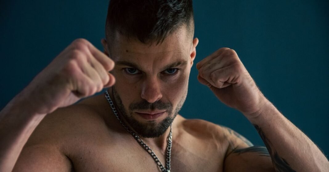 Strong and focused man posing with fists raised, showcasing power and determination in a studio setting.