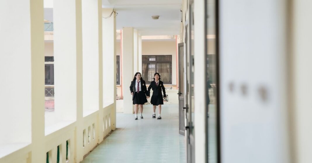 Two students in uniform walk through a bright school corridor.