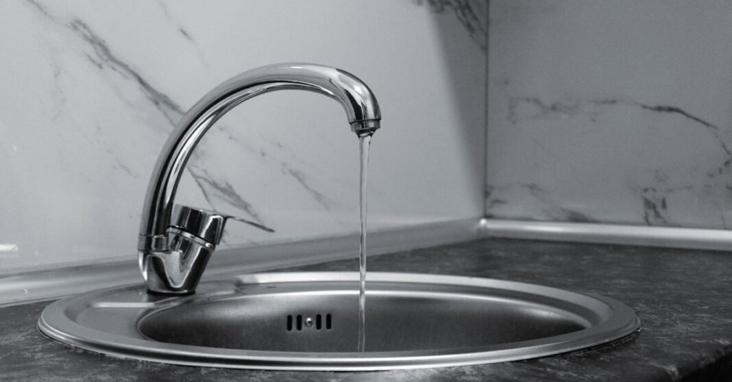 Chrome faucet with running water in a modern kitchen with marble countertop.