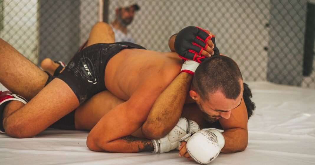 Intense moment of MMA fighters grappling inside an indoor cage.