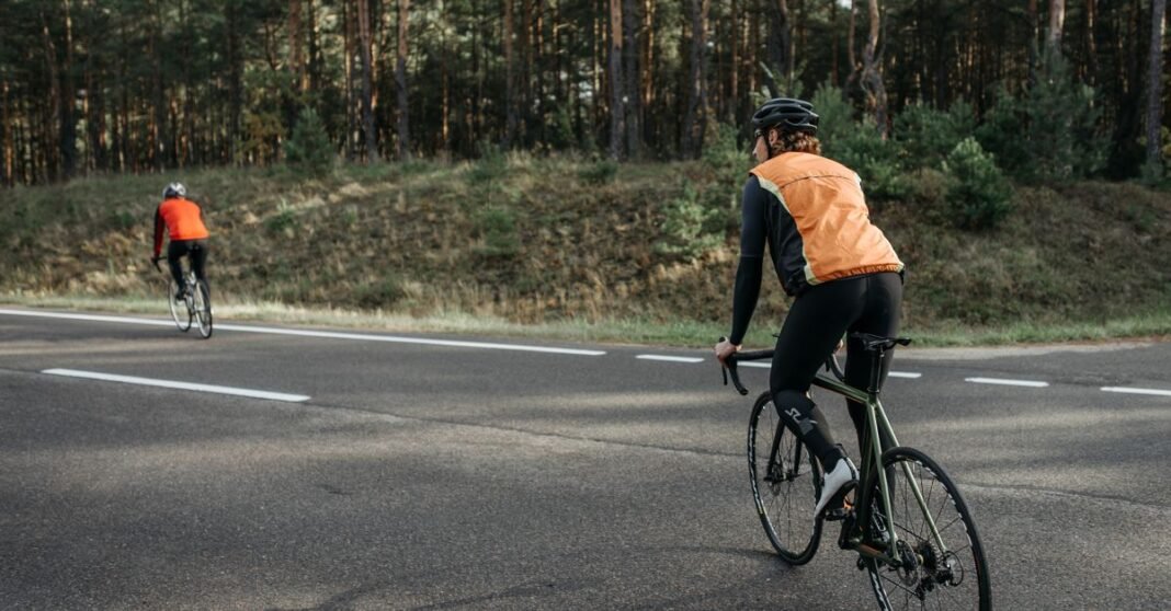 Two cyclists wearing reflective vests riding on a forest road, embracing nature and fitness.
