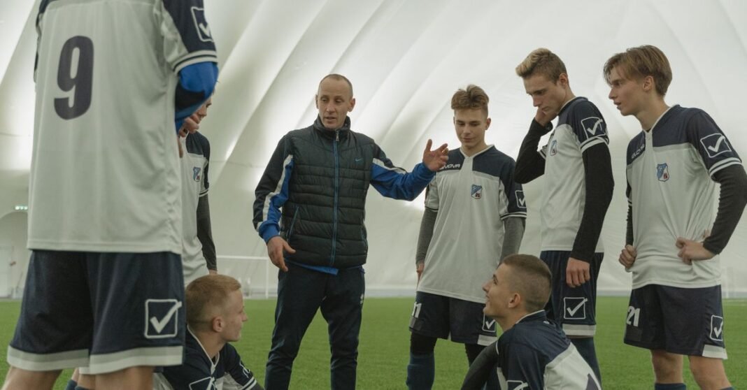A coach passionately instructs his soccer team during a practice session inside a sports dome.