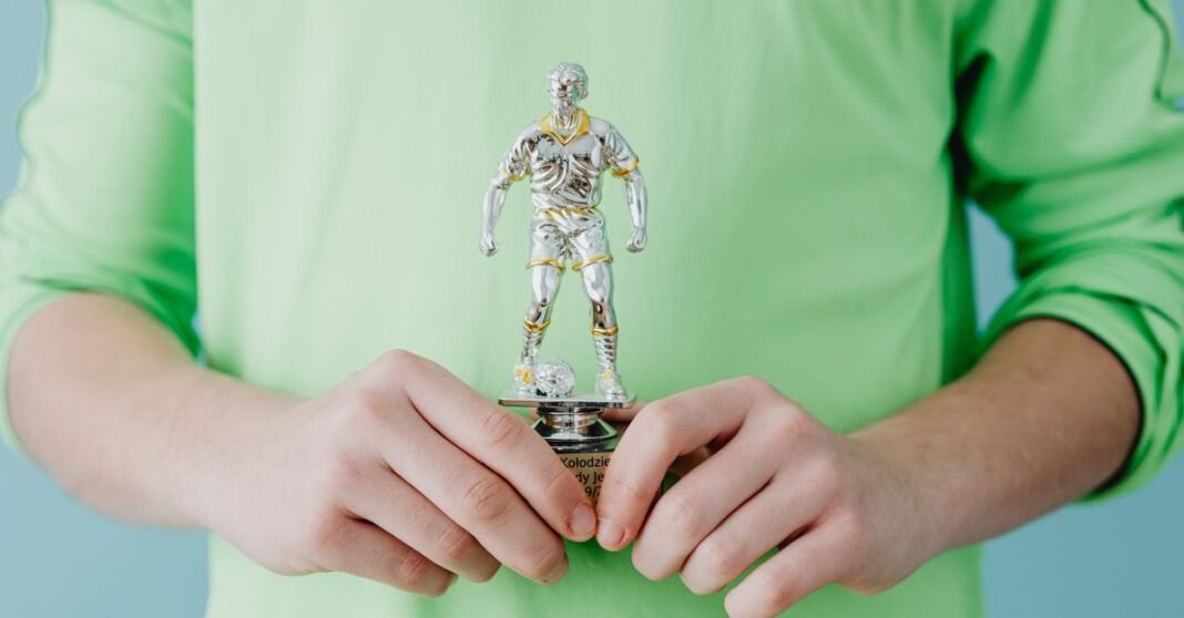 A person holding a silver soccer trophy against a blue background.