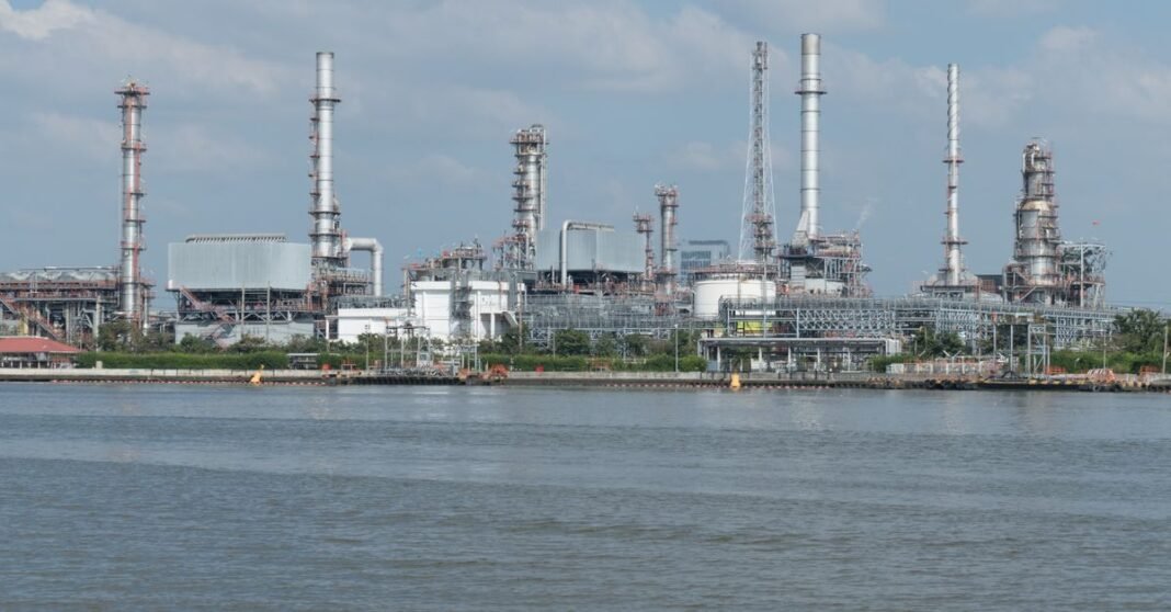 A large oil refinery complex next to the water with cloudy skies.