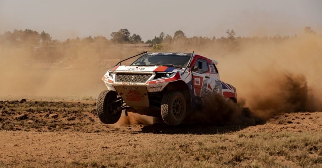 An off-road rally car accelerates through a dirt track, creating a lively dust trail.