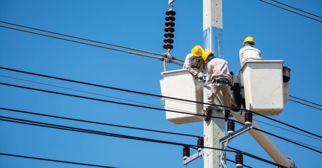 Electricians wearing safety gear work on power lines in Nakhon Ratchasima, Thailand.