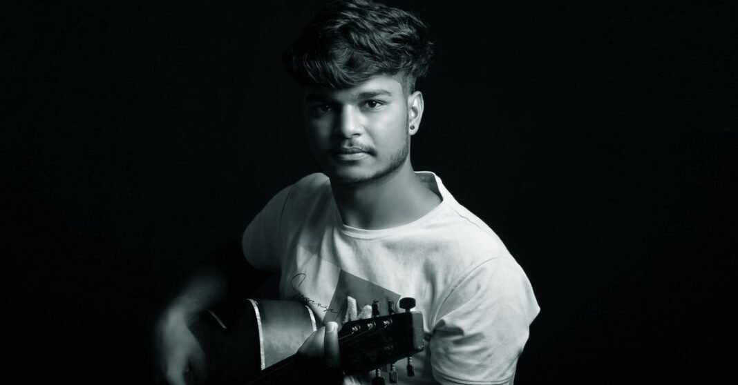 Moody portrait of a young man with a guitar, captured against a black background.