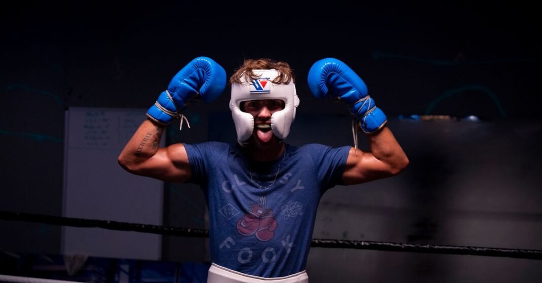 A young male boxer with gloves and helmet celebrating victory in a dimly lit gym.