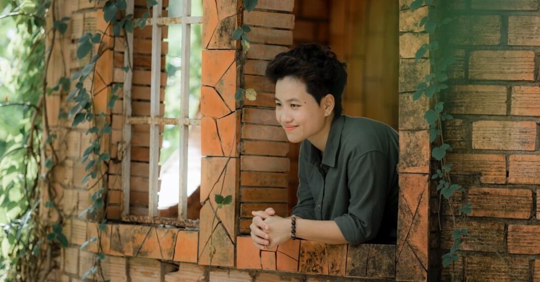 Person leaning out a window surrounded by ivy in a rustic brick building.