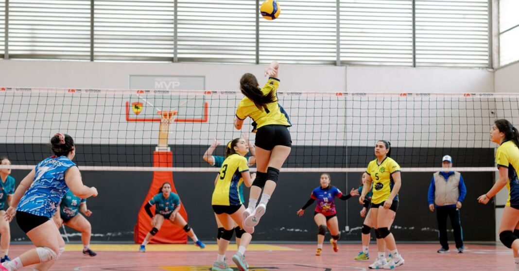Dynamic shot of a volleyball player jumping for a spike in an indoor game. Vibrant team uniforms add energy.