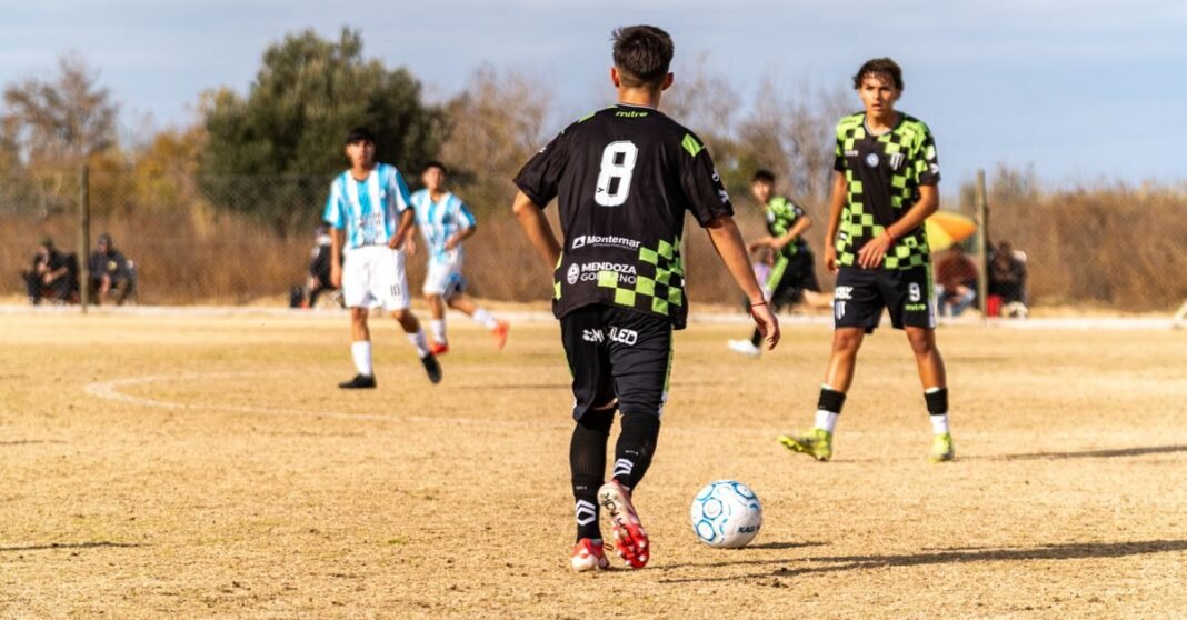 Boys playing soccer outdoors on a sunny day in team uniforms.