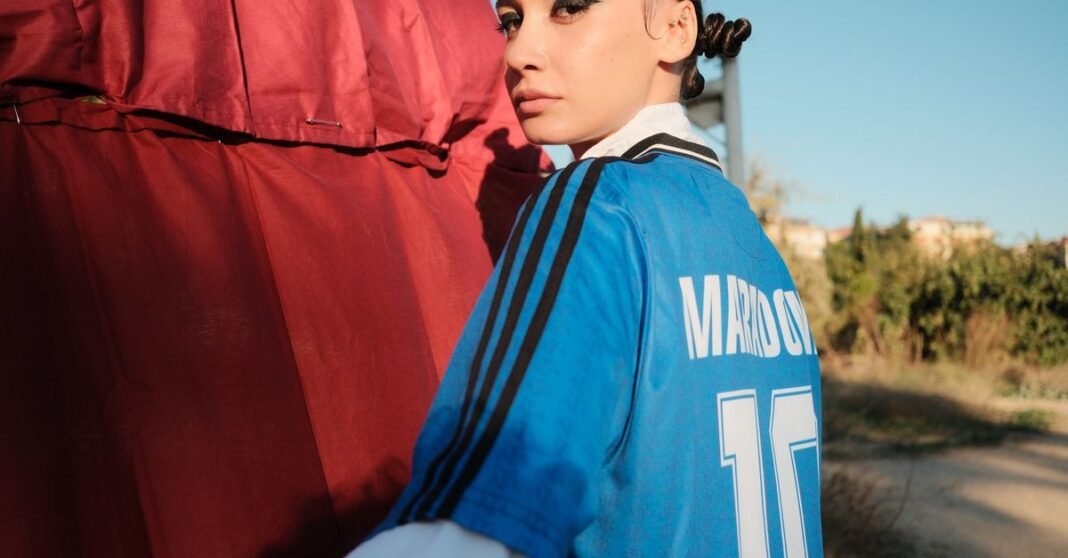 Woman in a retro soccer jersey stands outdoors, blending style and nostalgia.