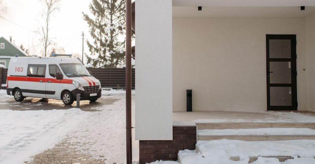 A parked ambulance near a snow-covered modern house during winter, displaying calm suburban life.