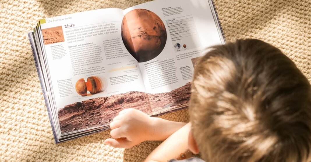 A child reading a book about Mars on a sunny carpeted floor, exploring space knowledge.