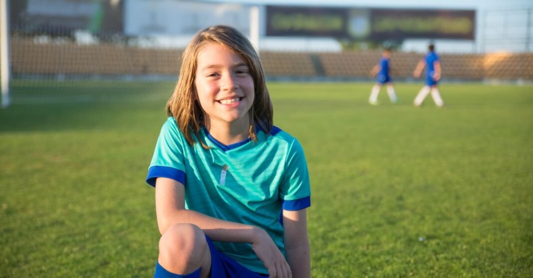 Young boy smiling on a soccer field in Portugal, wearing a sports jersey.