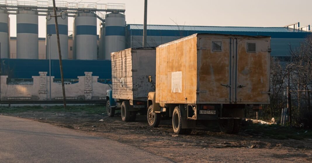 Two trucks parked near a factory in Salyan, Azerbaijan during daylight.