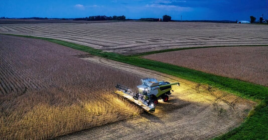 Drone captures a combine harvester working in Minnesota soybean fields at dusk.